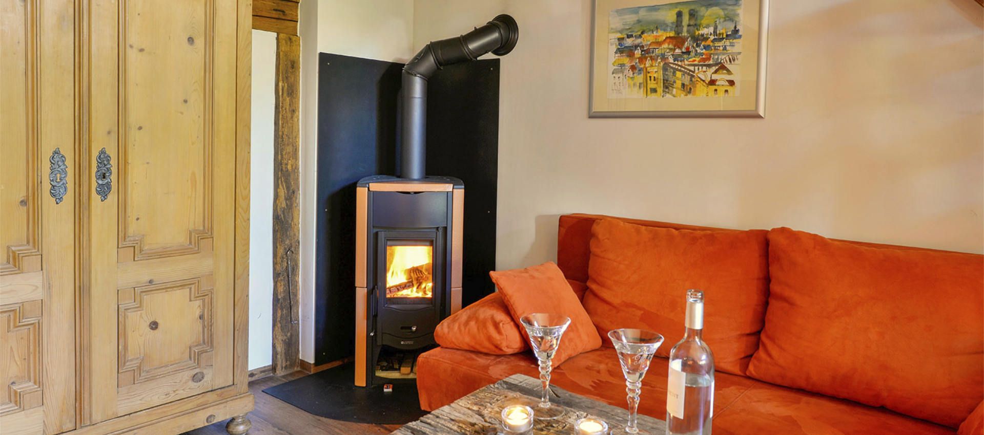 Die Kunstgalerie - orange Couch neben gemütlichem Kaminofen, darüber Kunstwerk